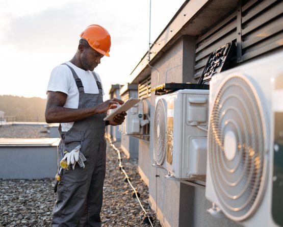 Attentive african american manager browsing internet on digital tablet while standing near modern cooling system on rooftop. Concentrated male working outdoors with beautiful sunset on background.